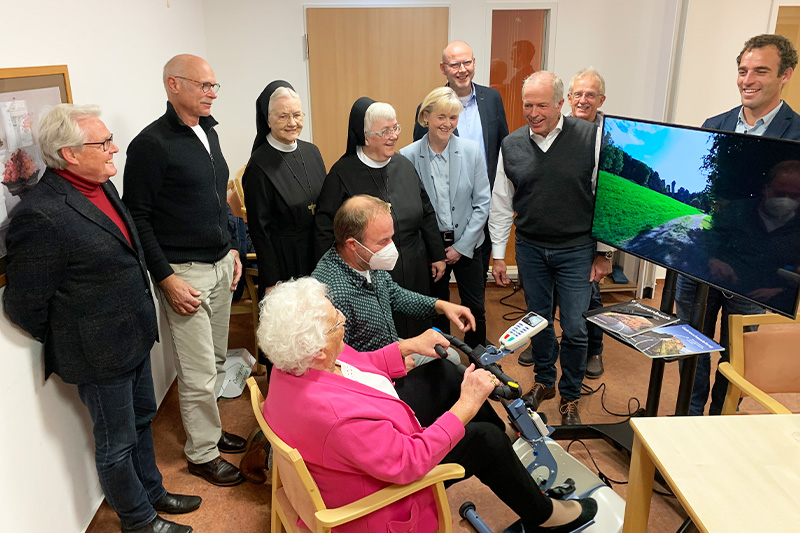 Rotarier Dr. Martin Rörig (2.v.l.), Schwester M. Raphaela vom Hofe, Geschäftsführerin des Altenheims, Einrichtungsleiterin Schwester M. Anke Junker, Rotarierin Claudia Artz, Andreas Cramer, Geschäftsführer des Altenheims, der aktuelle Rotary-Präsident Achim von Bremen, Rotarier Jürgen Jesper und hinter dem Bildschirm Thomas van der Ham von Bike Labyrinth. Vorne am Gerät sitzt Elisabeth Aniol vom Bewohner-Beirat und neben ihr Coen Verdouw von Bike Labyrinth. Alle Anwesenden waren geimpft und getestet. Foto: Mander